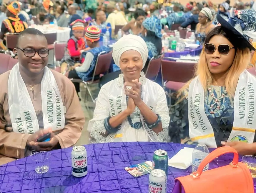 Trois délégués du Forum Mondial Panafricain portant l’écharpe du Forum, assis à une table lors de l’All Bamileke Convention aux États-Unis