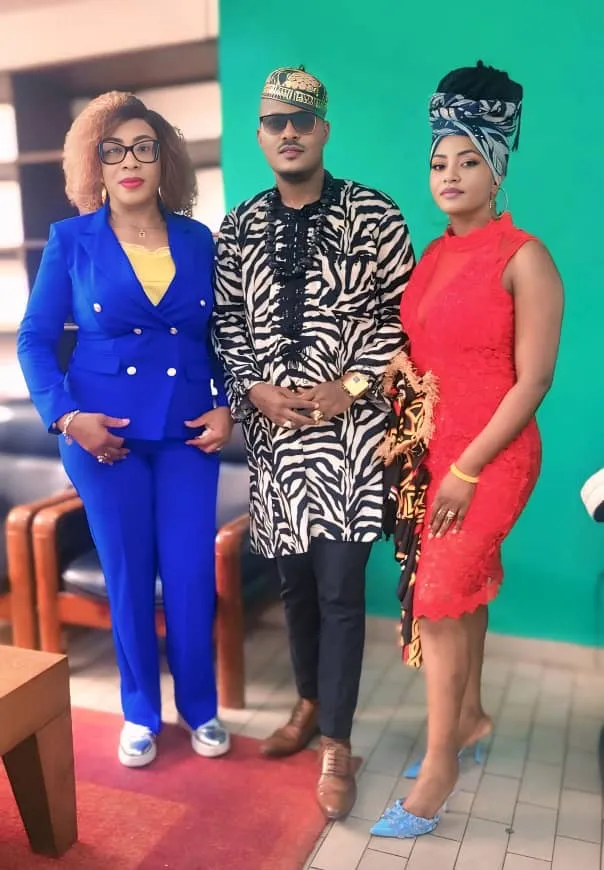 Joseph Kuika en tunique zébrée entre deux invitées, l’une en tailleur bleu, l’autre en robe rouge