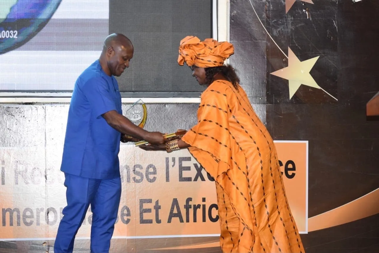 Présentation d’un trophée à une lauréate en robe orange, présentateur en costume bleu